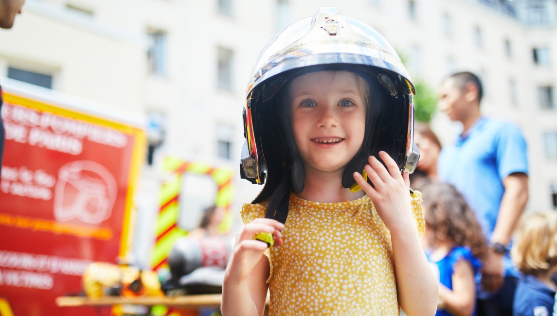 mała dziewczynka w hełmie strażackim uczy się, jak postępować w niebezpiecznych sytuacjach